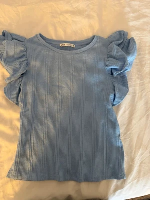 Blå ribbad topp med volangärmar Zara - Supersöt ljusblå topp från Zara med ribbad struktur och stora volangärmar. Storlek M men passar även S