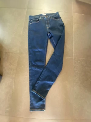 Mörkblå skinny jeans från GANT - Snygga mörkblå skinny jeans från GANT med klassisk femficksdesign och kontrastsömmar. Jeansen har en smal passform och är tillverkade i stretchigt denimtyg för extra komfort. Perfekta för en trendig och avslappnad look. Endast använda 2-3 gånger.