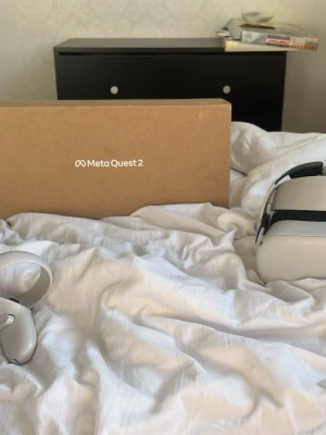 Meta Quest 2 VR-headset med kontroller - Meta Quest 2 VR-headset i vit plast med svarta detaljer och justerbart huvudband. Medföljer två ergonomiska handkontroller för maximal spelupplevelse. Perfekt för gaming, VR-upplevelser och sociala plattformar. Levereras i originalkartong.