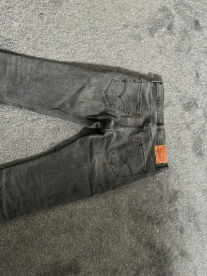 Grå Levi's jeans  - Säljer ett par grå jeans från Levi's med klassisk femficksdesign och raka ben. Jeansen har en snygg tvättad look och ikonisk läderpatch bak i midjan. Perfekta för en avslappnad och trendig stil.