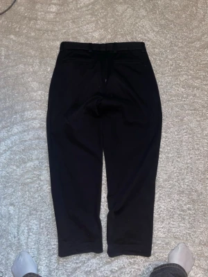 Svarta kostymbyxor med rak passform - Snygga svarta kostymbyxor med rak passform och bälteshällor. Klassisk design med knapp och dragkedja framtill. Perfekta för en stilren look. Materialet känns mjukt och har en lätt stretch för extra komfort.