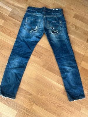 Blå dondup jeans med slitningar - Säljer ett par blå dondup jeans med slitningar och hål på både fram- och baksida. Perfekt för dig som gillar en avslappnad och trendig stil. Pris går att diskuteras.