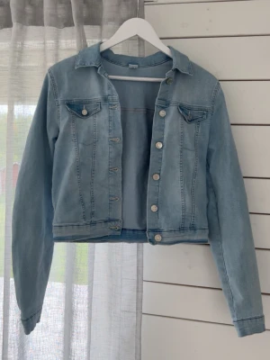 Ljusblå klassisk jeansjacka - Snygg ljusblå mjuk jeansjacka med raka sömmar och silverfärgade knappar. Två bröstfickor med lock och knapp, samt klassisk krage. Jackan har en croppad passform och långa ärmar med knapp vid ärmslut. Pris kan diskuteras! Hör av er vid funderingar!😊