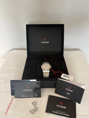 Tudor 28400 34mm - i mint condition - Stilren klocka från Tudor i silverfärgat stål med klassisk länkarmband och romerska siffror på urtavlan. Klockan kommer med Tudor låda och full set med papper. Även en extra link tillkommer. Klockan har en garanti fram till 2030. I mint condition. Riktigt snygg klocka för vardagen eller särskilda tillfällen.