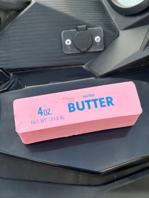 Stor rosa squishy 'BUTTER' - Säljer ett stort rosa squishy leksak utformat som ett smörpaket med texten '4oz BUTTER SALTED' i blått.  är rektangulärt och har en rolig design som liknar ett riktigt smörpaket. Perfekt som kul skrivbordstillbehör eller present.