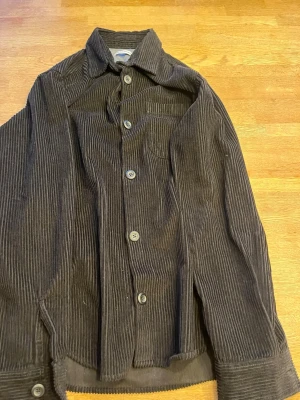 Brun manchester overshirt Jack & Jones - Snygg brun overshirt från Jack & Jones i mjuk manchester. Skjortan har klassisk krage, knappstängning framtill och en bröstficka. Perfekt lager på lager-plagg med avslappnad passform och trendig retrostil. Aldrig använd 