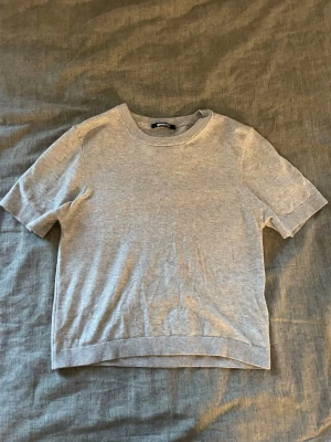 Ljusgrå kortärmad topp - En enkel och stilren ljusgrå topp med korta ärmar och rund hals. Tillverkad i mjukt material som känns skönt mot huden. Perfekt att matcha med jeans eller kjol för en clean look.