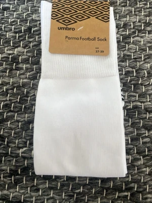 Vita fotbollsstrumpor från Umbro - Säljer ett par vita Parma Football Sock från Umbro i storlek 37-39. Strumporna är långa och tillverkade i ett lätt och slitstarkt material, perfekta för fotbollsträning eller match. De har ribbstickad kant och anatomisk passform för bästa komfort.