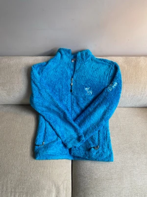 Blå fluffig ziptröja från Abercrombie & Fitch - Säljer en blå, supermjuk och fluffig ziptröja från Abercrombie & Fitch. Tröjan har dragkedja framtill och två fickor med dragkedja. Broderad logga på bröstet och tryck på ärmen. Perfekt för kalla dagar och riktigt cozy vibes.