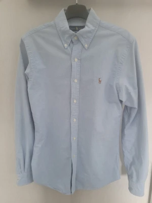 Ralph Lauren skjorta  - Klassisk ljusblå skjorta från Ralph Lauren med broderad logga på bröstet. Slim fit-modell med knappar hela vägen och lång ärm. Perfekt för en stilren look. Endast testad. Ny. Hör av er vid frågor.