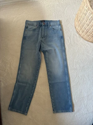 Wrangler ljusblå raka jeans - Helt nya ljusblå jeans från Wrangler i modellen Toughlite. Klassisk femficksdesign med raka ben och normal midja. Jeansen har en snygg tvättad look och är tillverkade i slitstarkt denimtyg. Perfekta för en avslappnad och stilren vardagsoutfit.