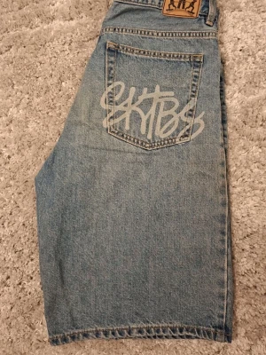 Baggy jeansshorts - Säljer ett par ljusblå, baggy jeansshorts från sweet sktbs med graffiti-inspirerad logga på baksidan. Perfekta för dig som gillar streetwear och avslappnad stil.