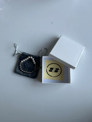 Pärlarmband från Smuggler96 - Snyggt armband från seams med halva bandet i vita pärlor och andra halvan i silvriga metallpärlor. Kommer med original ask och tygpåse. Perfekt accessoar för att lyfta din stil med en mix av klassiskt och modernt.
