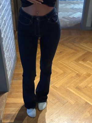 Mörkblå bootcut jeans - Snygga mörkblå bootcut jeans med hög midja och klassiska fem fickor. Jeansen har en smal passform upptill och lätt utsvängda ben. Perfekta för dig som vill ha en tidlös och trendig look. Inga synliga märken eller detaljer.