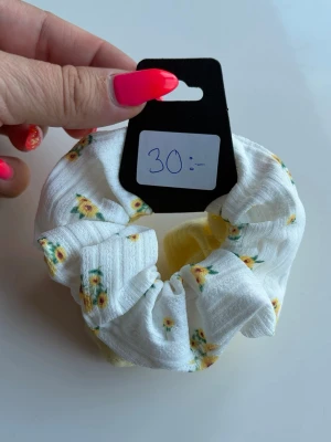 Gul och vit scrunchie med blommor - Två scrunchies i ett set, en i ljusgul ribbad trikå och en i vit tyg med små gula blommor. Perfekt för att piffa till håret med en söt och somrig look. Mjukt material som är skonsamt mot håret. Nya ej använda 