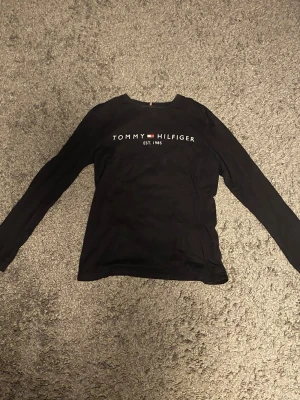 Svart Tommy Hilfiger långärmad T-shirt - Storlek:164 cm, är i bra skick och inköpt från kids brand store.