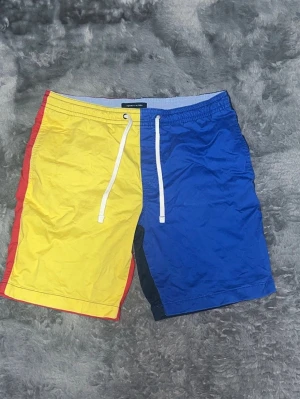Tommy Hilfiger Colorblock Shorts (Nyskick) - Sjukt snygga och bekväma shorts i klassisk Hilfiger-design (gul, blå, röd). Oanvända, nytvättade och i perfekt skick med alla tvättlappar kvar. • Skick: 10/10 – Helt som nya. • Passform: Skön resår i midjan med snörning.  Kolla in mina andra annonser!