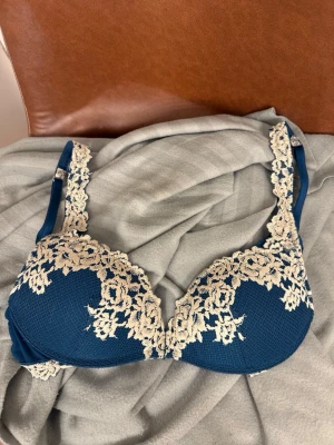 Blå intimissimi bh - Snygg blå/grön bh med vadderade kupor och dekorativa vita spetsdetaljer över kuporna och axelbanden. Bh:n har ett elegant blommönster i spetsen och justerbara axelband för bästa passform. Materialet känns mjukt och bekvämt mot huden. 