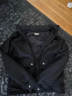 Svart vindjacka från Zadig&Voltaire  - Stilren svart vindjacka från Zadig&Voltaire med hög krage och dragkedja framtill. Jackan har två stora fickor med lock och tryckknappar samt justerbara ärmslut. Jättefint skick enda nackdelen är att hänguglan håller på att åka av men det är lätt att fixa.