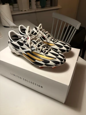 Adidas fotbollsskor limited edition - Säljer ett par Adidas fotbollsskor från Limited Collection med svartvitt geometriskt mönster och guldiga detaljer på sidorna. Skorna har snörning, låg profil och är tillverkade i syntetmaterial för bästa grepp på planen. Perfekta för dig som vill sticka ut på matchen. Nummer 14! 