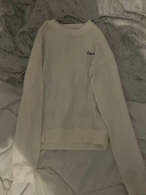 Vit sweatshirt med broderad text - En stilren vit sweatshirt med rund hals och lång ärm. På bröstet finns en liten broderad text där det står 'love' i svart. Tröjan har ribbade muddar vid ärmslut och nederkant. Perfekt för en avslappnad och enkel look.