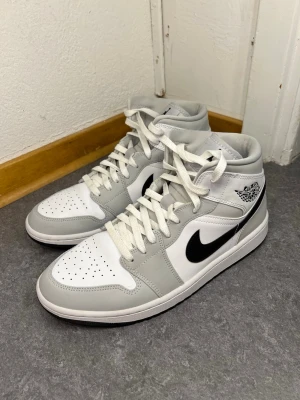 Autentiska Nike Air Jordan 1 Mid vit/grå/svart - Snygga Nike Air Jordan 1 Mid sneakers i vitt, ljusgrått och svart. Välvårdad och i mycket bra skick, använd ett fåtal gånger. Köpt på Merchsweden, kvitto finns. Inköpspris:3499kr Mittpris:1900kr
