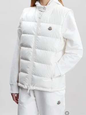 Moncler väst - Snygg vit dunväst från Moncler med hög krage och dragkedja framtill. Västen har Monclers ikoniska logga på bröstet och två sidofickor med dragkedja. Nypris ligger på 11 000 kr. Självklart är den äkta💗