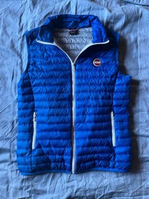 Blå dunväst från Colmar - Snygg blå dunväst från Colmar med vit dragkedja och två fickor framtill. Västen har quiltad design och står ut med sitt klassiska Colmar-märke på bröstet. Perfekt för lager-på-lager och ger en sportig vibe till din outfit.