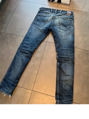 Mörkblå slitna jeans från replay - Säljer ett par mörkblå jeans från replay med slitningar och hål vid knät. Klassisk femficksmodell med dragkedja och knapp. Jeansen har en tvättad look och är tillverkade i denim. Perfekta för en avslappnad och trendig stil.