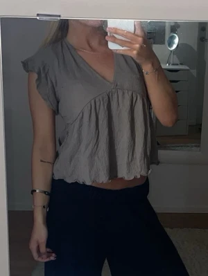 Brun grå  v-ringad blus med volang - Brun grå  med v-ringning och volangdetaljer. Aldrig använd 💕