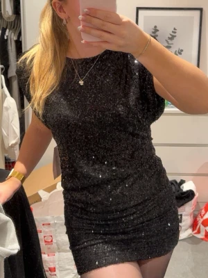 Svart glittrig kortklänning - Säljer en svart kortklänning med glittriga paljetter. Lätt axelvaddering också! Aldrig använd med prislapp kvar i strl S🥰