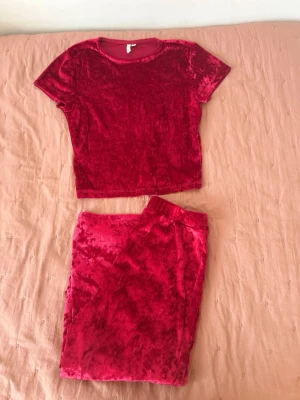 Rött velourset med t-shirt och byxor från Nelly - Mysigt loungewear-set i röd velour med kortärmad t-shirt och matchande byxor med resår i midjan. Perfekt för chill hemma eller när du vill vara extra bekväm. Mjuk och glansig känsla i materialet.