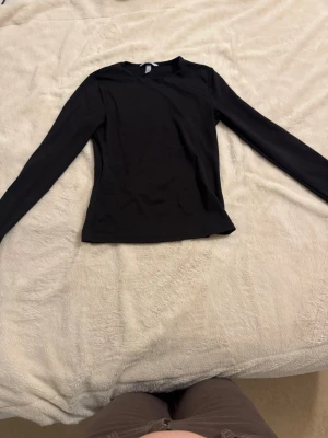 Svart långärmad topp från H&M - En stilren svart långärmad topp från H&M. Toppen har en klassisk rund halsringning och är figurnära i modellen. Perfekt att matcha med jeans eller kjol för en enkel och snygg look.