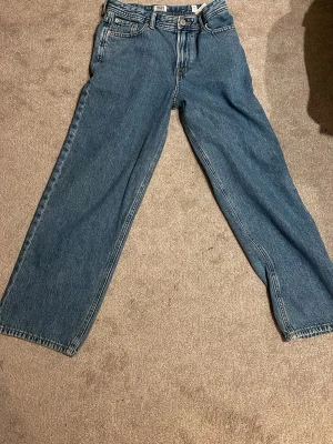 Blå raka jeans från Jack& Jones  - Säljer ett par klassiska blå jeans från Jack& Jones med rak passform och hög midja. Jeansen har fem fickor, knappgylf och är tillverkade i kraftig denim. Perfekta för en avslappnad och trendig look.
