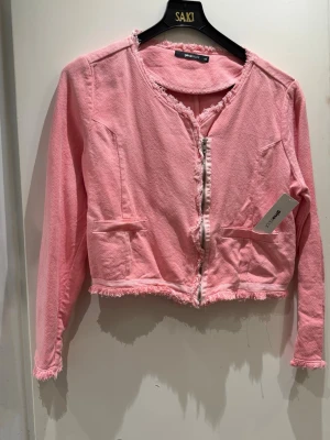 Rosa cardiganjacka från Gina Tricot - Trendig rosa cardiganjacka från Gina Tricot med råa kanter och rund halsringning. Jackan har långa ärmar, två dekorativa fickor framtill och dragkedja. Tillverkad i ett mjukt tyg som ger en avslappnad men ändå stylish look.