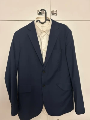 Arket Mörkblå kostym - Snygg mörkblå kostymset från ARKET. Kavajen och skjortan är i storlek 50 medan byxorna är i storlek 48. Väldig fin kostym av hög kvalité i 100% ull.