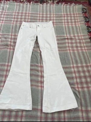 Vita utsvängda jeans från Jane Norman - Säljer ett par vita jeans från Jane Norman med riktigt snygg utsvängd passform. Klassisk femficksmodell med bälteshällor och silverfärgade detaljer. Perfekta för dig som vill sticka ut med en retroinspirerad look. De är väldigt lågmidjade och säljer vidare då de inte passar, måtten finns på bilderna🩷🩷