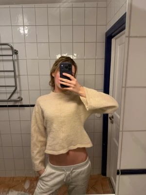 Beige stickad tröja Gina Tricot - Mysig beige stickad tröja från Gina Tricot med rund halsringning och breda ärmar. Tröjan har ribbade muddar vid halsen och nederkanten, och är tillverkad i ett mjukt material som passar perfekt för kyligare dagar.