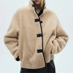 Beige pälsjacka med skinndetaljer från Mango storlek S  - Säljer en beige pälsjacka från mango i storlek S med hög krage och svarta knappar samt svarta kantdetaljer. Hårtyg. Päls effekt. Rak design. Oversize design. Hög krage. Långärmad. Två framfickor. Knäppning på framsidan. Ny med prislapp 