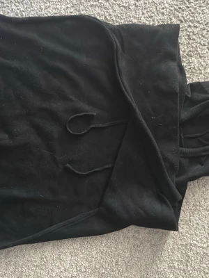 100% Kashmir hoodie - En klassisk svart hoodie med huva och dragsko. Hoodien har en enkel design utan synliga loggor eller tryck, ribbade muddar vid ärmslut och nederkant samt en stor magficka framtill. Perfekt för en avslappnad och stilren look.