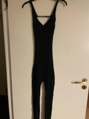 Svart tight jumpsuit med cut-out(ord pris 600kr) - Snygg svart jumpsuit från EGO med smala axelband och en trendig cut-out detalj vid bröstet. Tight passform och långa ben, perfekt för dig som gillar en stilren och modern look. Stretchigt material som sitter skönt på kroppen.