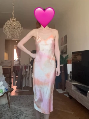 Midiklänning pastellfärgad slipklänning silkesklänning - Säljer en lång slipklänning i pastelliga toner av rosa, orange och vitt. Klänningen har tunna axelband och en mjuk, glansig finish som ger en lyxig känsla. Perfekt för sommarens alla tillfällen och har en smickrande, figurnära passform. Oanvänd.