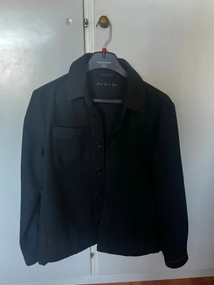 Svart overshirt från D’once de la sense - Stilren svart overshirt från D’once de la sense med klassisk krage, knappstängning och en bröstficka. Perfekt lager-på-lager-plagg med enkel design och mjukt material. Passar till många olika outfits. Swish betalning endast!!! Tveka inte vid frågor och funderingar!!!!