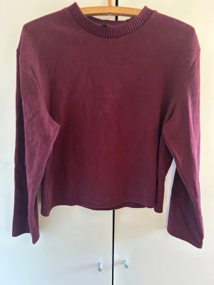 Vinröd stickad tröja - Vinröd stickad tröja med rund halsringning och långa ärmar. Tröjan har en enkel, rak passform och ribbad kant vid halsen. Perfekt för lager på lager och höstmys.