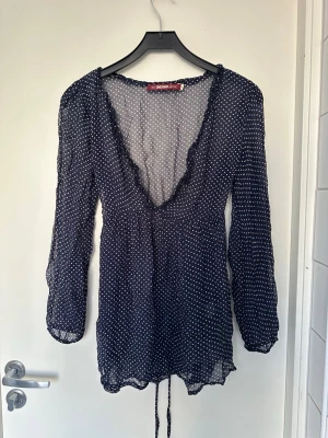 Mörkblå prickig blus med volang - Söt mörkblå blus från Odd Molly med vita små prickar, djup v-ringning med volangkant och knytband i midjan. Blusen har långa ärmar och är gjord i ett tunt, transparent material som ger en luftig känsla.