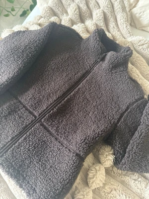 Mörkbrun teddyjacka med dragkedja - Mysig mörkbrun teddyjacka med hög krage och hel dragkedja framtill. Jackan har en boxig passform och är gjord i fluffigt, mjukt teddy-material som håller dig varm. Perfekt för kyliga dagar och enkel att styla till olika outfits.