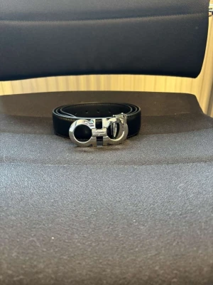 Svart skärp från Salvatore Ferragamo - Snyggt svart skärp från Salvatore Ferragamo med ikoniskt silverfärgat spänne i metall. Klassisk och stilren design som passar till många olika outfits. Skärpet är gjort i slätt skinn och har exklusiv känsla.