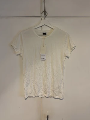 Vit basic t-shirt från GinaTricot  - En klassisk vit t-shirt från GinaTricot i mjuk bomull. Modellen har rund halsringning och korta ärmar, perfekt för en clean och enkel stil. Passformen är normal och tyget känns lätt och skönt mot huden.