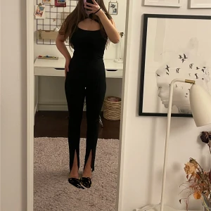Svarta leggings med slits fram - Säljer ett par svarta leggings med hög midja och trendig slits framtill vid bensluten. Tight passform som framhäver benen och stretchigt material för skön känsla. Perfekta till sneakers eller klackar för en snygg look. Jag ör 170 cm💕