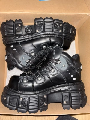 New rock tank storlek 43 - Tunga svarta stövletter från New Rock med rejäl platåsula och industriella detaljer i metall. Skorna har snörning, rund tå och coola nitar längs sidorna. Tillverkade i läder med robust gummisula och tydlig logga under sulan. Perfekta för en alternativ och edgy stil.